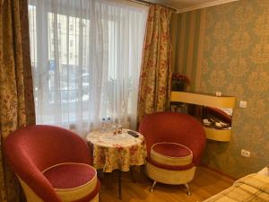 ペルミにあるHotel Khozyayushkaの椅子2脚、テーブル、窓が備わる客室です。