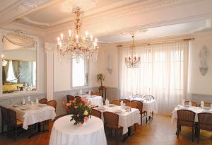 una sala da pranzo con tavoli bianchi e un lampadario di Hôtel Gloria & Avenue a Lourdes