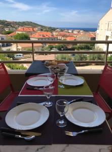 a table with plates and wine glasses on a balcony at Jardins de Quatrina in Propriano