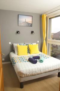 a bed with yellow and blue pillows and a window at APPARTEMENT ENTRE GENÈVE ET CHAMONIX AU PIED DES MONTAGNES in Cluses