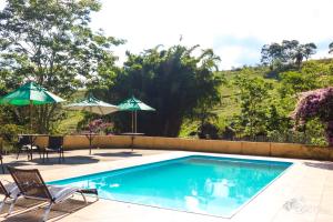 a swimming pool with two chairs and two umbrellas at Pousada e Restaurante Victórios in Caeté