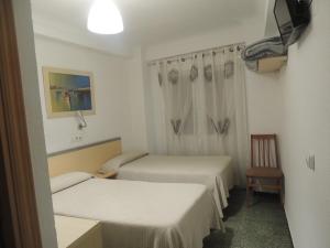 Una pequeña habitación con dos camas y una silla. en Hostal Cumbre, en Zaragoza