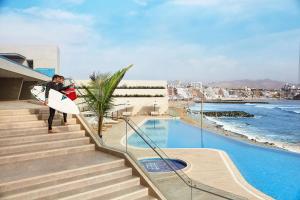 a person holding a surfboard walking down stairs next to a pool at Vive - Descansa - Disfruta in San Bartolo