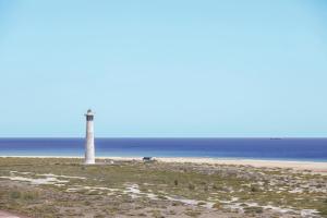 a lighthouse on a beach next to the ocean at Palm Garden in Morro del Jable
