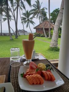 a plate of fruit on a table with a drink at Rockside Cabanas Hotel in Unawatuna
