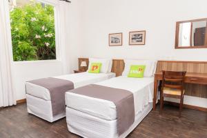 two beds in a room with a desk and a window at VOA Hotel União in Caxambu