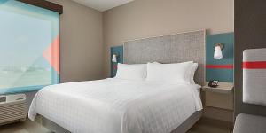 avid hotels - Detroit - Warren, an IHG Hotel في وارين: غرفة نوم بسرير ابيض ونافذة