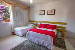 1 dormitorio con 2 camas con almohadas rojas y ventana en Hotel Pousada Casa Tasca, en Bento Gonçalves