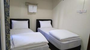 2 camas en una habitación con sábanas y almohadas blancas en Axlite Hotel en Taiping