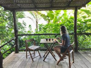 una mujer sentada en una mesa en una cubierta en Casinha romantica frente para o mar, en Ilhabela
