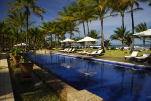 a swimming pool with chairs and umbrellas and palm trees at Txai Resort in Itacaré