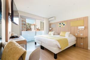 a bedroom with a bed and a desk and a window at Hôtel Hélios in Juan-les-Pins