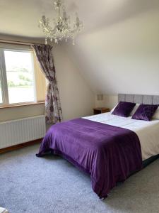 a bedroom with a bed with purple sheets and a window at Cloneymore Self Catering House in Cushendun