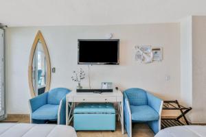 a room with two blue chairs and a tv on a wall at Sunshine & Oceanfront Serenity in Daytona Beach Shores