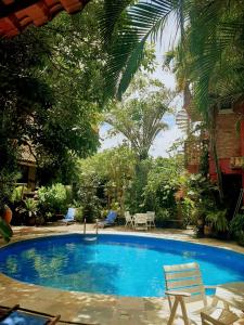 a large blue swimming pool with two chairs and trees at Pousada Pilar in Arraial do Cabo