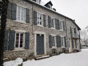 a stone building with black shutters on it in the snow at Le domaine des 3 marmottes Chambres d' hôtes in Cierp