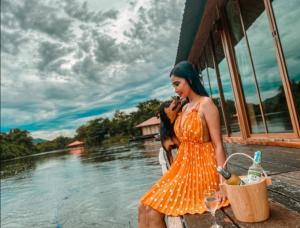 Kodaun River Kwai Resort في مدينة كانشانابوري: امرأة ترتدي ثوب برتقالي تقف بجوار جسم من الماء