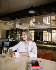 a woman sitting at a table with a cup of coffee at 7 days hotel in Almaty