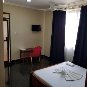 een kamer met een bed, een tafel en een rode stoel bij Prideinn Lodge Kigamboni in Dar es Salaam