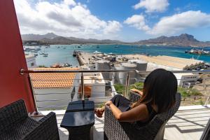 a woman sitting on a balcony looking at a harbor at Blue Marlin Hotel in Mindelo