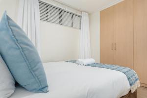 białe łóżko z niebieską poduszką i oknem w obiekcie Dockside Apartments w Kapsztadzie
