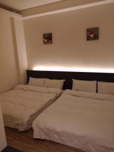 two beds in a room with white sheets at Tilon Hotel in Pingtung City