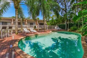 a pool with chairs and palm trees in front of a house at Central Noosa location, Noosa Heads in Noosa Heads