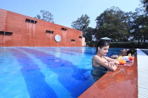 a woman sitting in a swimming pool with a man taking a picture at Aveo by Amatra, Gateway to Corbett in Kāshīpur