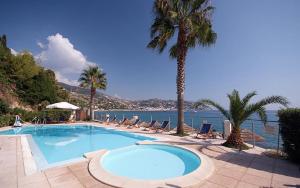 a swimming pool with chairs and palm trees next to the water at Residence Baia La Ruota in Bordighera