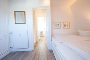 a white bedroom with a bed and a mirror at C-Haus Constanze, App 46 in Wenningstedt