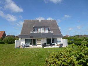 una casa bianca con il tetto grigio su un campo verde di Haus Nordseegruss, App 4 a Wenningstedt