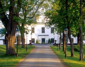 a road in front of a white house with trees at Häringe Slott in Västerhaninge