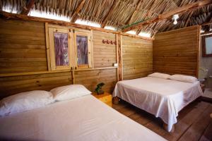 Duas camas num quarto com paredes e janelas de madeira em Cabañas El Arca em Tierra Bomba