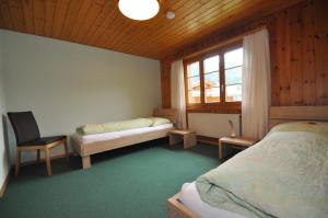 a bedroom with two beds and a window and a chair at Ferienwohnungen Hotel Alpina in Adelboden