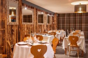 un restaurante con mesas blancas, sillas y espejos en l'Ecrin des Neiges, en La Joue du Loup