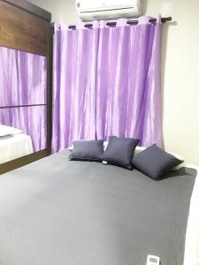 Quarto - Condomínio في ماكابا: غرفة نوم مع ستارة أرجوانية وسرير مع وسائد