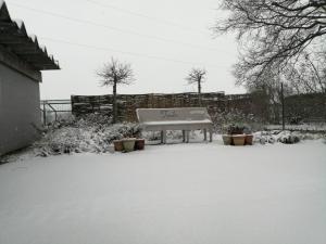 um banco sentado na neve num quintal em tende em Deerlijk