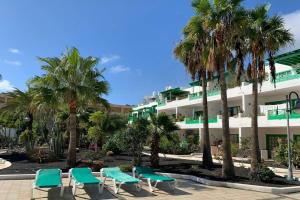 a building with chairs and palm trees in front of it at Apartamento Bastian Casas Verdes in Costa Teguise