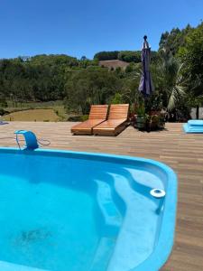 a swimming pool with two chairs and an umbrella at Sítio com Piscina e Vista a 12km de Treze Tílias in Ibicaré