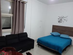 a bedroom with a bed and a couch and a window at Kitnet Guarujá Pitangueiras (sem garagem) in Guarujá