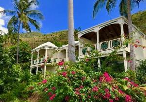 una casa blanca con flores rosas y palmeras en Sugar Mill Hotel, en Great Carrot Bay