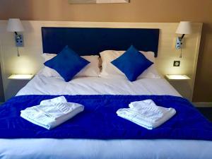 a white bed with blue pillows and towels on it at Hôtel Les Alizés in Puget-Théniers