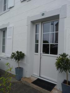 une porte blanche sur une maison blanche avec deux plantes en pot dans l'établissement Gîte la presqu'ile, à Portbail