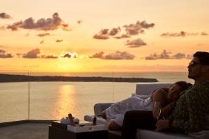 Um casal sentado num sofá a ver o pôr-do-sol. em Charisma Suites em Oia