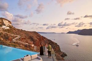 a group of people standing on the edge of a cliff near the water at Charisma Suites in Oia