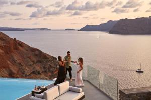 a bride and groom standing on the edge of a house overlooking the water at Charisma Suites in Oia
