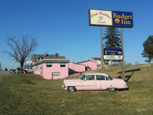 un coche rosa estacionado en un campo junto a una señal en Budget Inn Natural Bridge, en Natural Bridge
