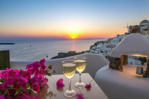 due bicchieri di vino seduti su un tavolo con un tramonto di Kastro Oia Houses a Oia