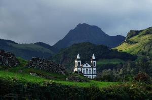a white house on a green hill with mountains at Casa do Avô Silva in Santa Cruz das Flores
