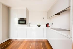 a white kitchen with white cabinets and a wooden floor at Gran View Apartments in Madrid
